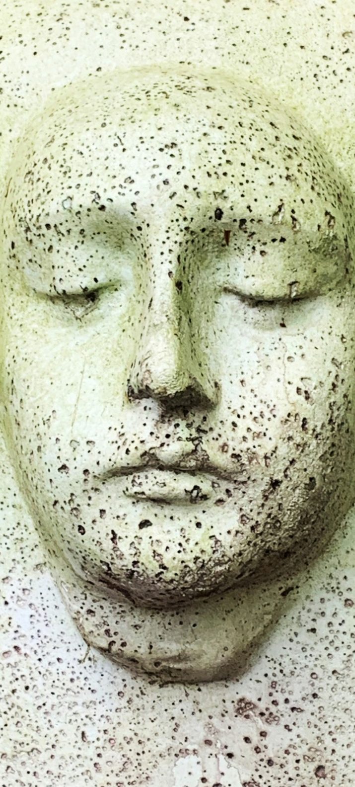 Hellgrüne Steinskulptur eines Gesichts mit feinen Details und ruhigem Ausdruck aus einem porösen Steinblock geschlagen.
