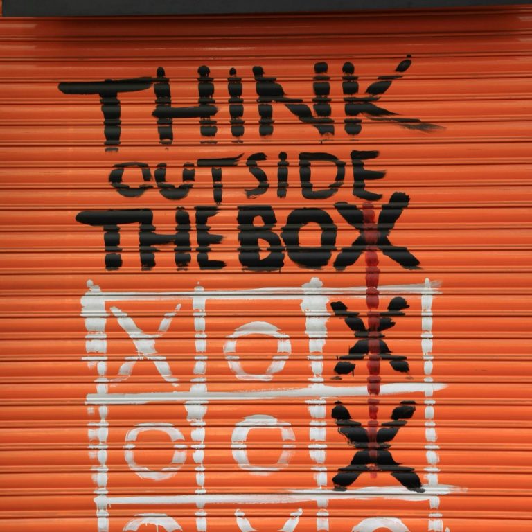 Graffiti auf orangefarbenem Hintergrund mit dem Text "THINK outside THE box" und dem Tic-Tac-Toe-Spiel mit einem Kreuz außerhalb vom Kreuz.