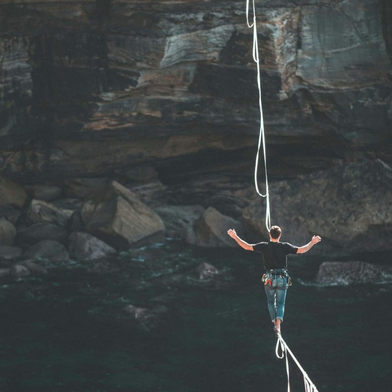Ein Mensch balanciert auf einer Slackline über Wasser, umgeben von Felsen.