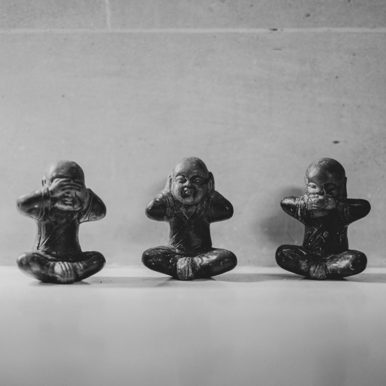 Drei kleine, sitzende Mönchsfiguren mit einzeln verschlossenen Augen, Ohren und Mund in schwarz-weißer Darstellung.