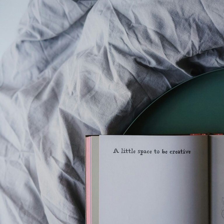Ein afugeschlagenes Buch mit dem Text "A little space to be creative" in einem dunkelgrünen, runden Tablett auf einem hellgrauen Leinentuch.