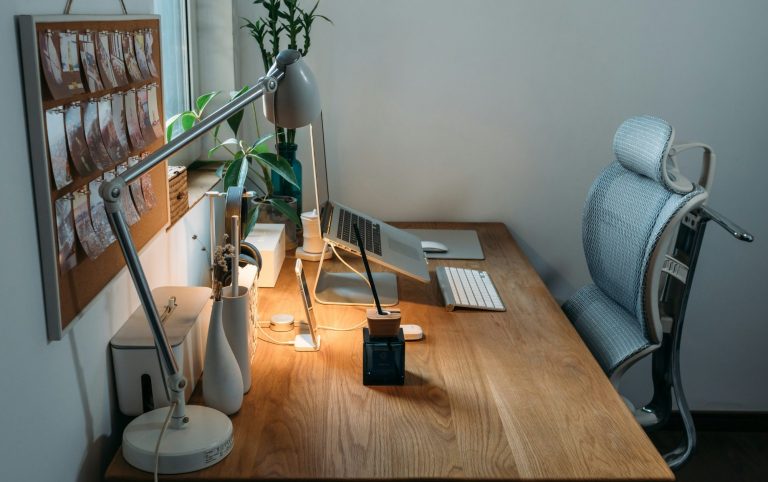 Hellblaue Schreibtischumgebung mit Pflanzen, Laptop und moderner Schreibtischlampe auf einer Eichentischplatte.